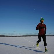 Man running on a snowy field in winter under clear blue skies.