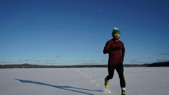 Man running on a snowy field in winter under clear blue skies.