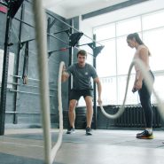 Man and woman exercising with battle ropes indoors.
