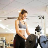 Smiling woman in gym adjusting dumbbells for a workout routine.