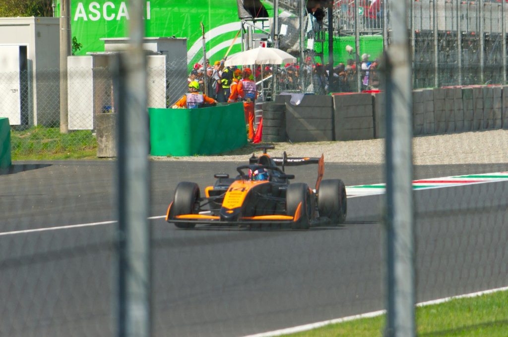 A race car speeds down a track with spectators watching.