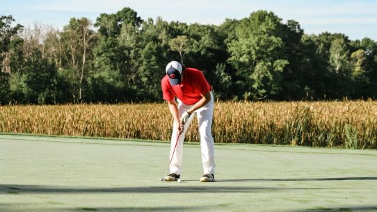 a man in a red shirt and white pants playing a game of golf