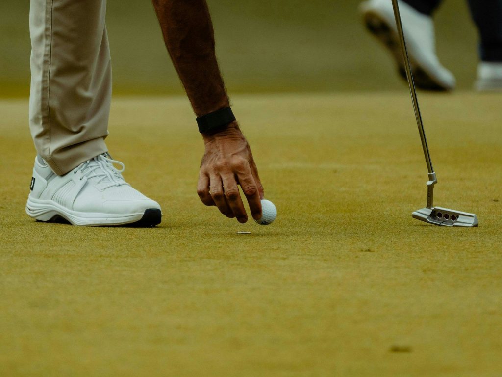 A golfer is picking up the ball on the green.