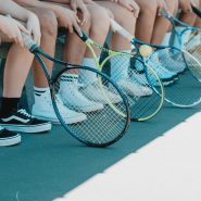 person in black and white nike sneakers holding blue and white tennis racket