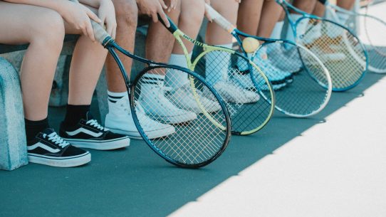 person in black and white nike sneakers holding blue and white tennis racket