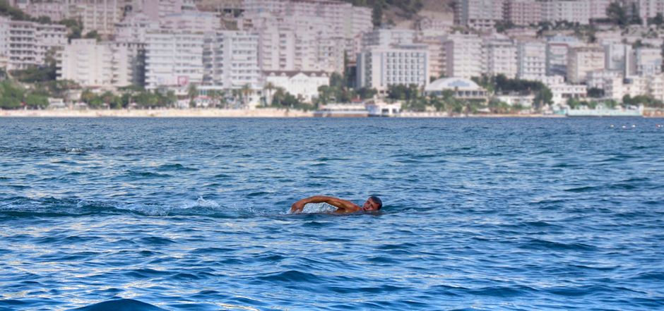 Man swimming in the Adriatic Sea with Sarandë, Albania skyline.