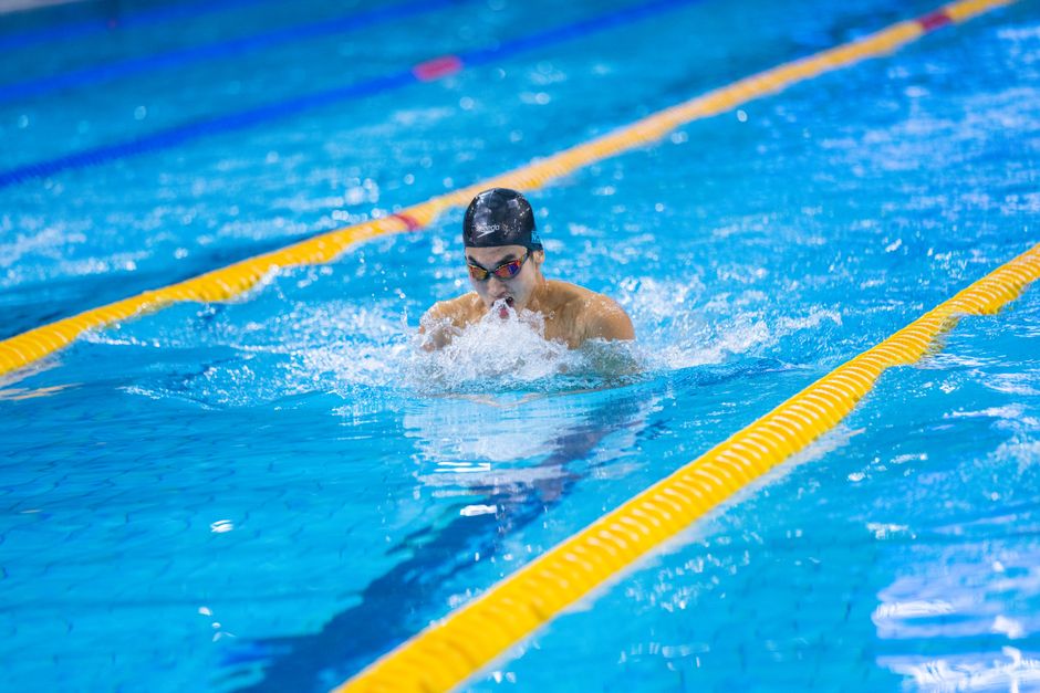 A focused adult male swimmer performing the breaststroke in an indoor swimming pool during the day.