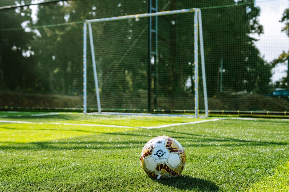 Close-up of a soccer ball on a grass field with a goalpost in the background, outdoor setting.