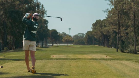 Bir golfçü ağaçlarla çevrili sahada vuruş yaparken