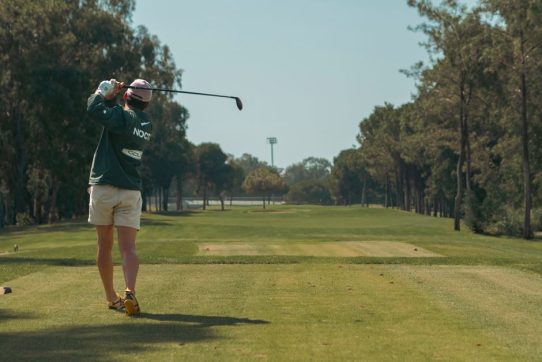 Bir golfçü ağaçlarla çevrili sahada vuruş yaparken