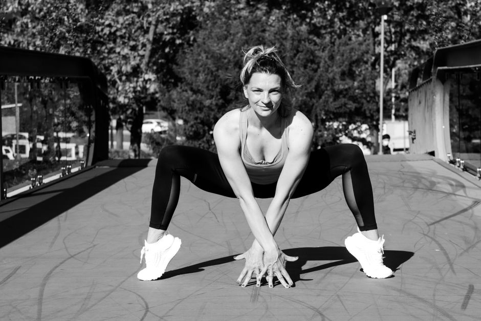 Woman in sports attire doing a crouching stretch on a bridge, black and white photo.