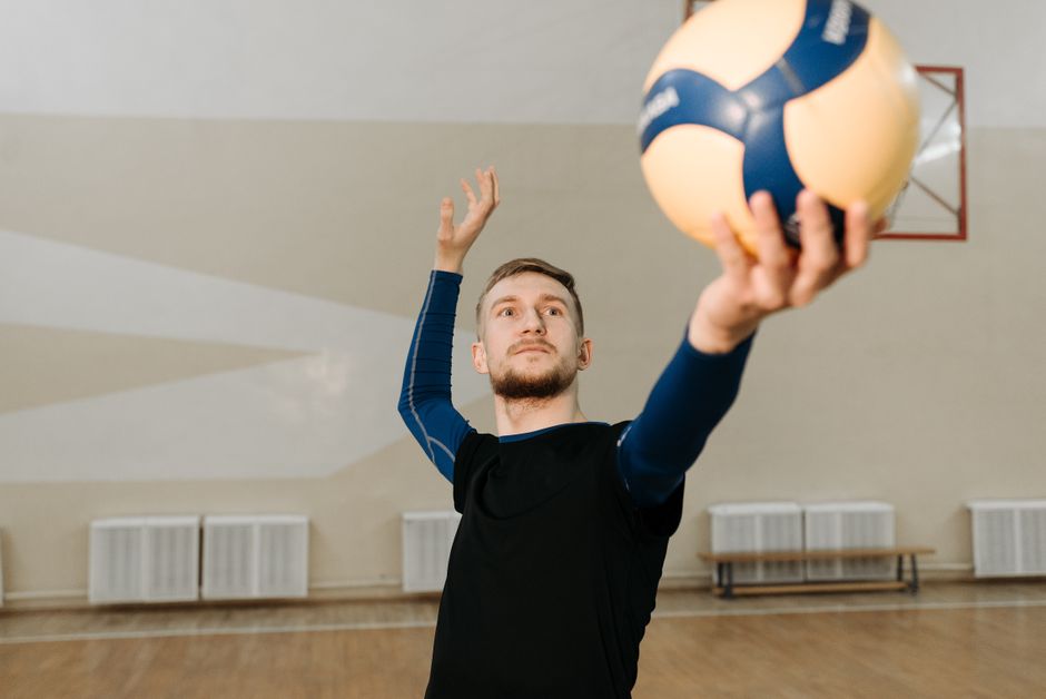 A male volleyball player getting ready to serve in an indoor gym setting.