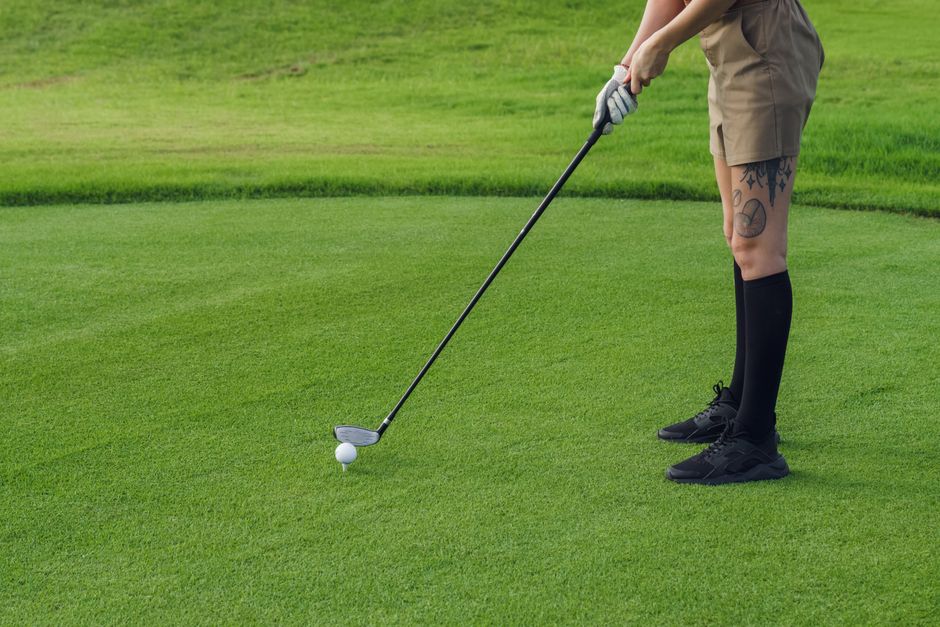 A golfer with tattoos prepares to putt on a lush golf course green.
