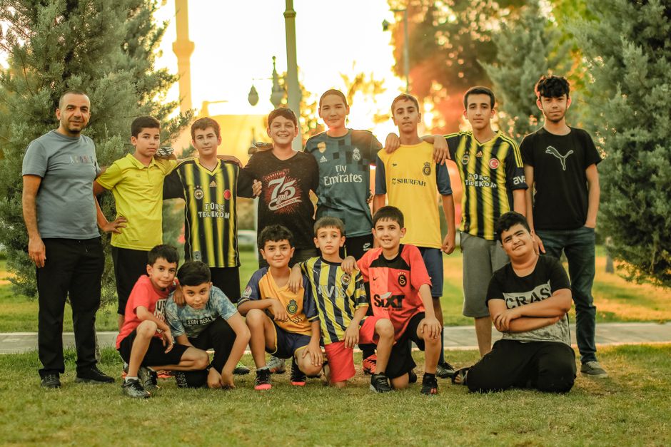 Group of teenagers and their coach posing for a soccer team photo in a park.