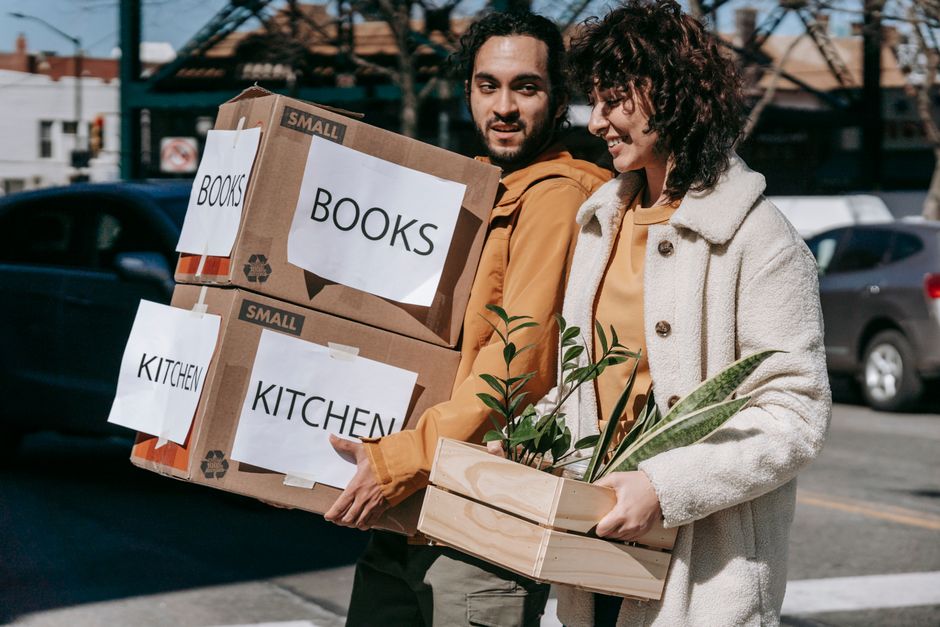 Joyful couple carrying boxes and plants while relocating to a new neighborhood on a sunny day.